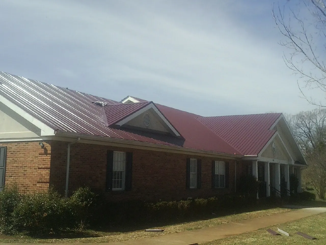 Red metal roof with gabled entries on a long brick building, from a Hail Damage Roof Repair job in Atco