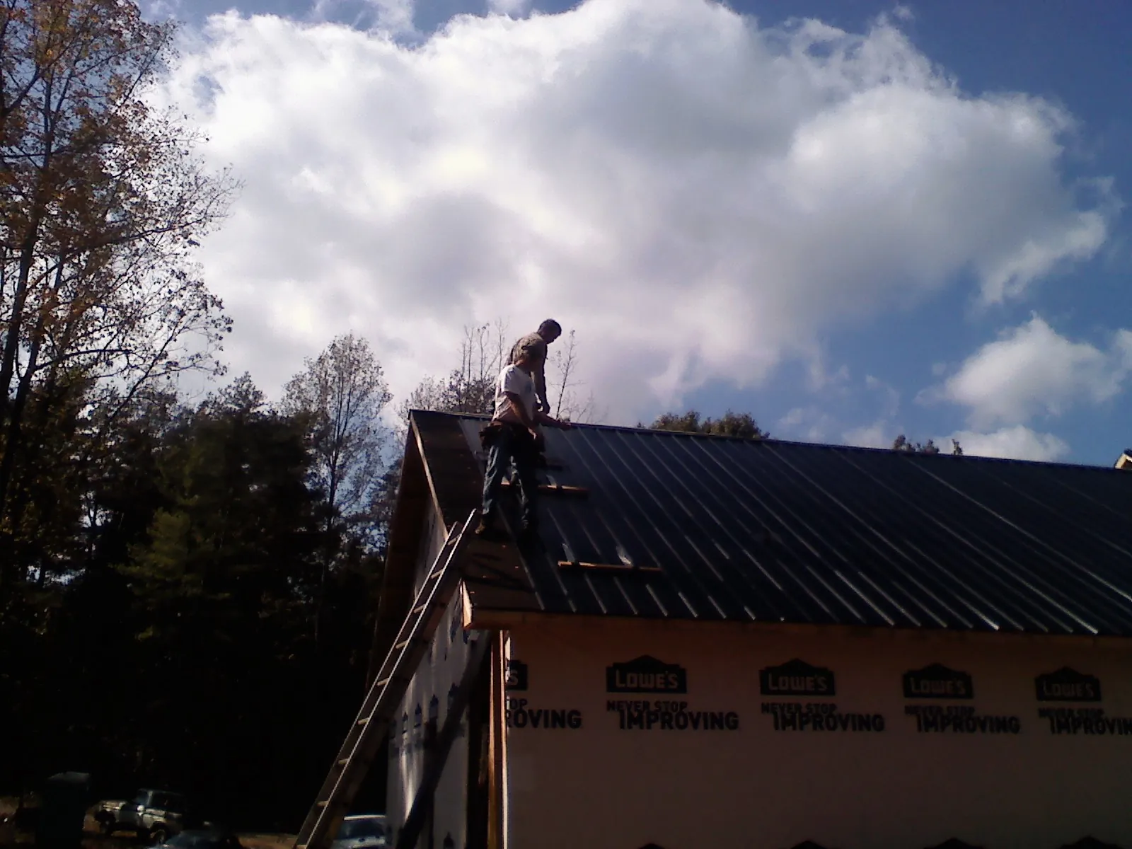 Roofer fastening dark metal panels high against a cloudy sky, from a Roof Inspection job in Atco