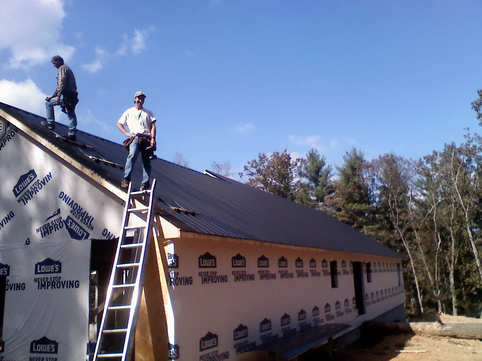 Two roofers standing on a long dark metal roof over a wrapped building in Atco