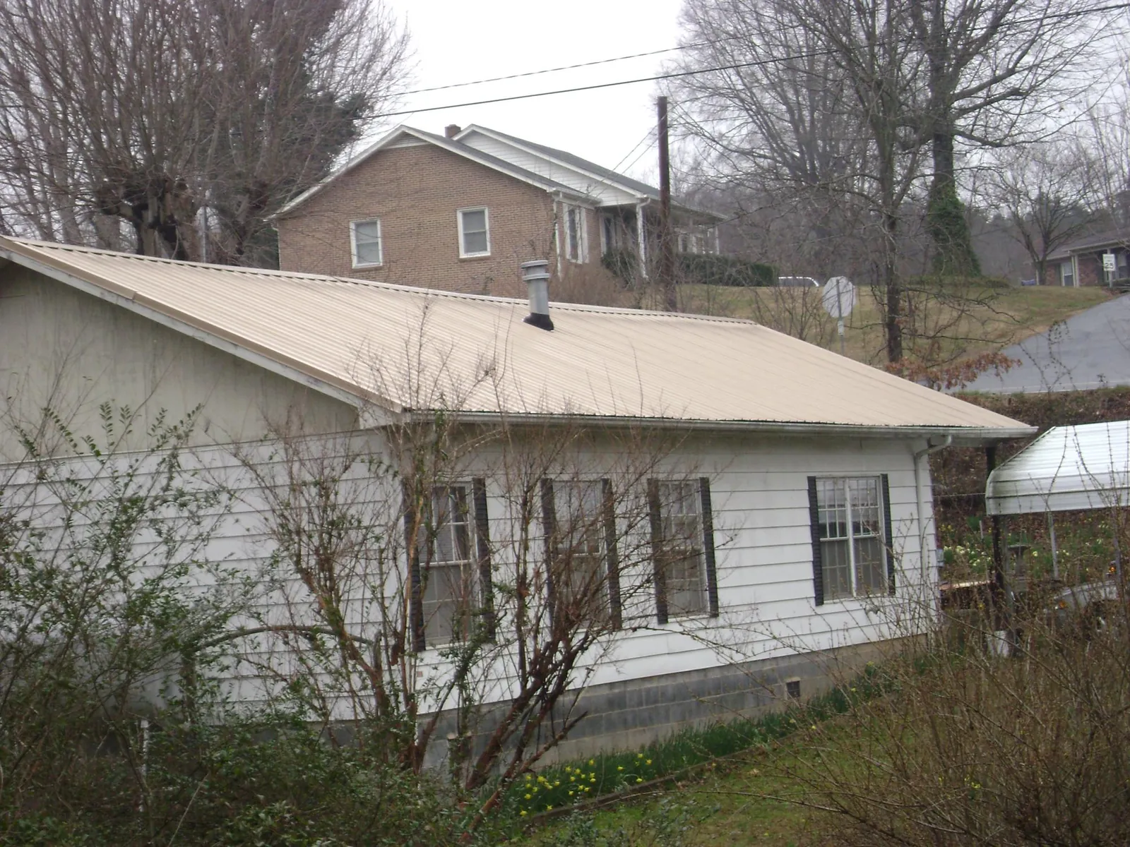 Tan metal roof on a white sided house set into a hillside — Commercial Roofing by Roofing Brothers in Atco